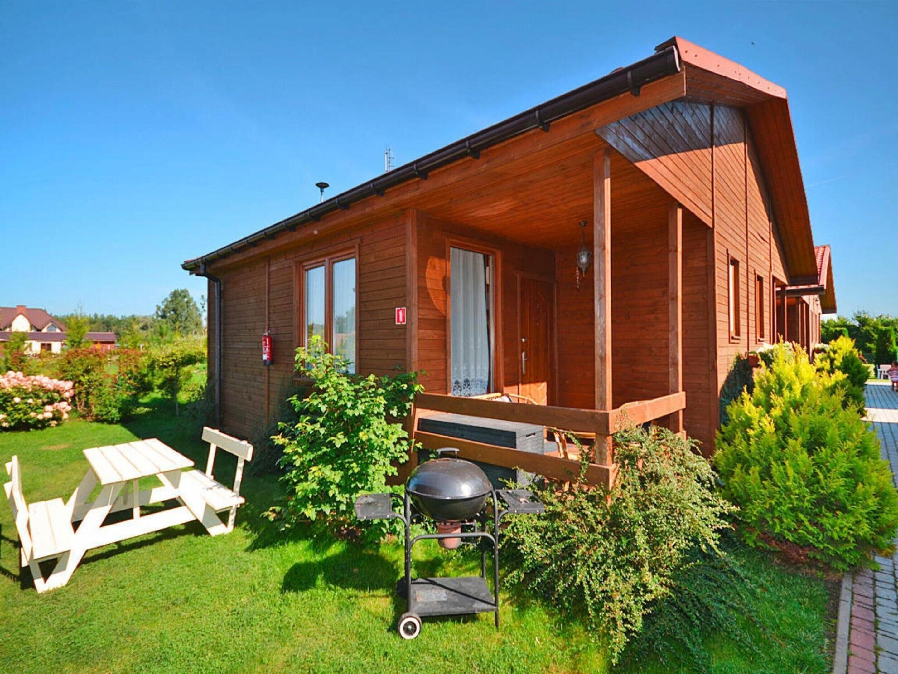 Eine Holzhütte mit überdachter Veranda, Grill und Picknicktisch im Garten.