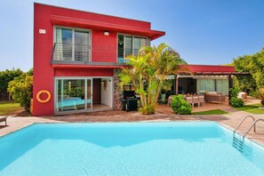 Une maison moderne à deux étages dotée d’une piscine, de mobilier d’extérieur et d’un espace barbecue.
