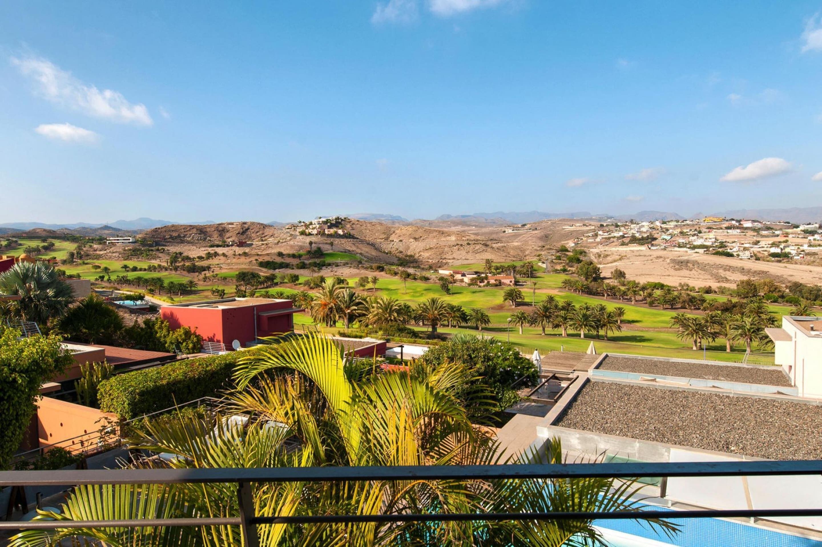 A residential area with a view of distant hills, a swimming pool, and a red building.