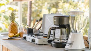 Una encimera de cocina con estufa a gas, cafetera, licuadora y una piña.