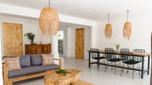 Una sala de estar moderna con un sofá, una mesa de centro de madera, una mesa de comedor con sillas y lámparas colgantes de mimbre.