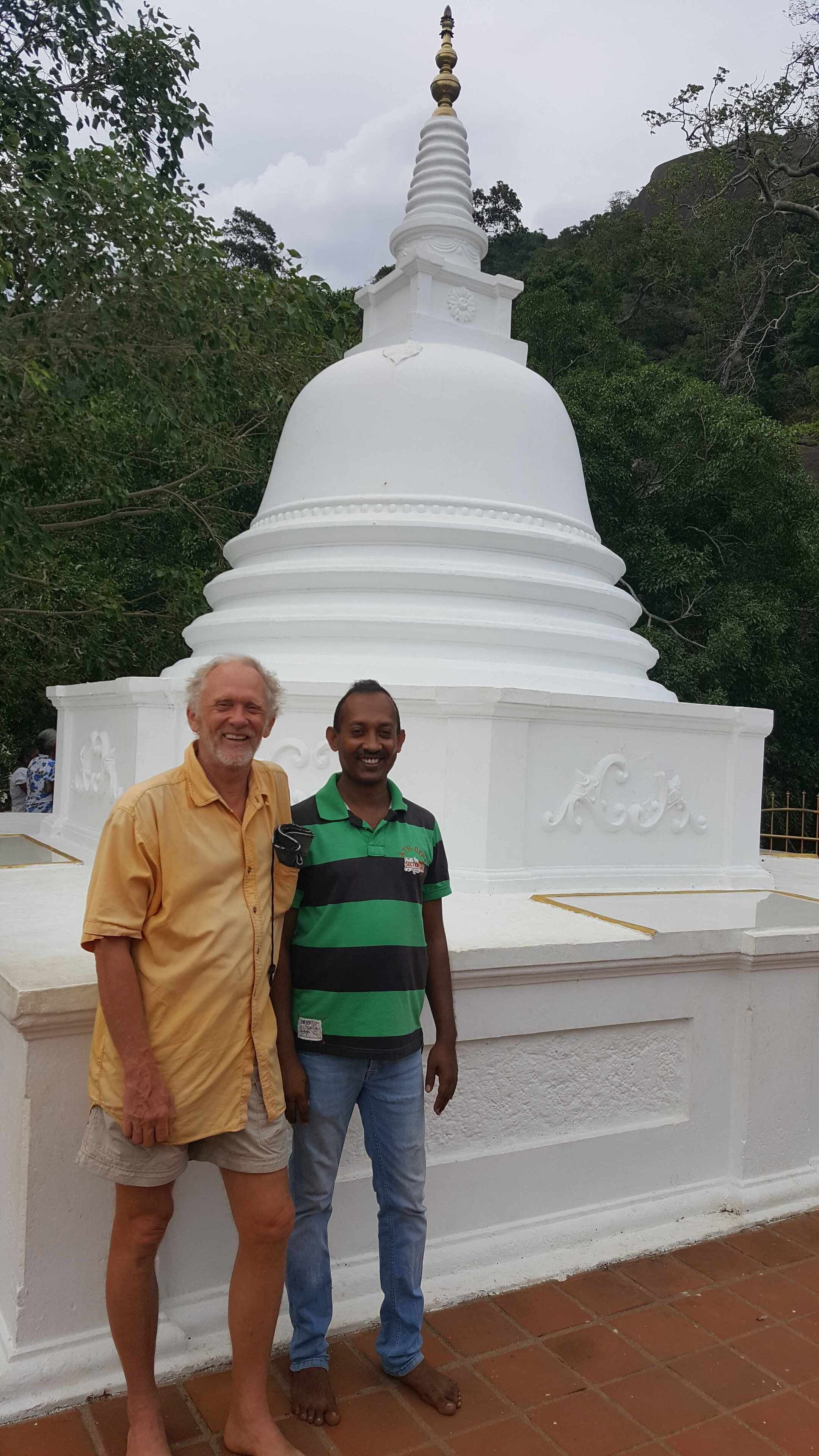 Un stupa blanc surmonté d’une coupole dorée, entouré de verdure.