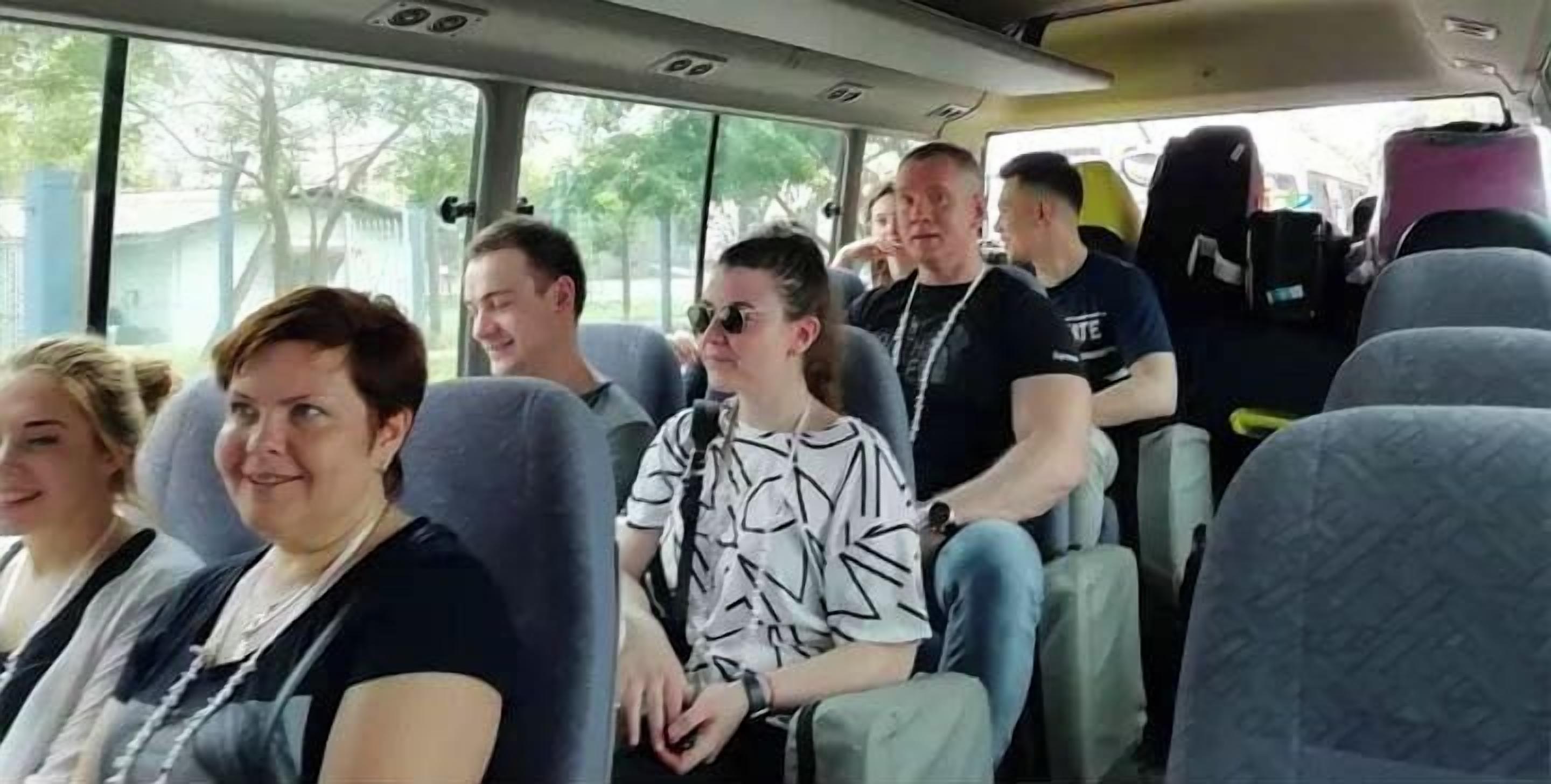 Een businterieur met passagiers, ramen en bagagevakken.