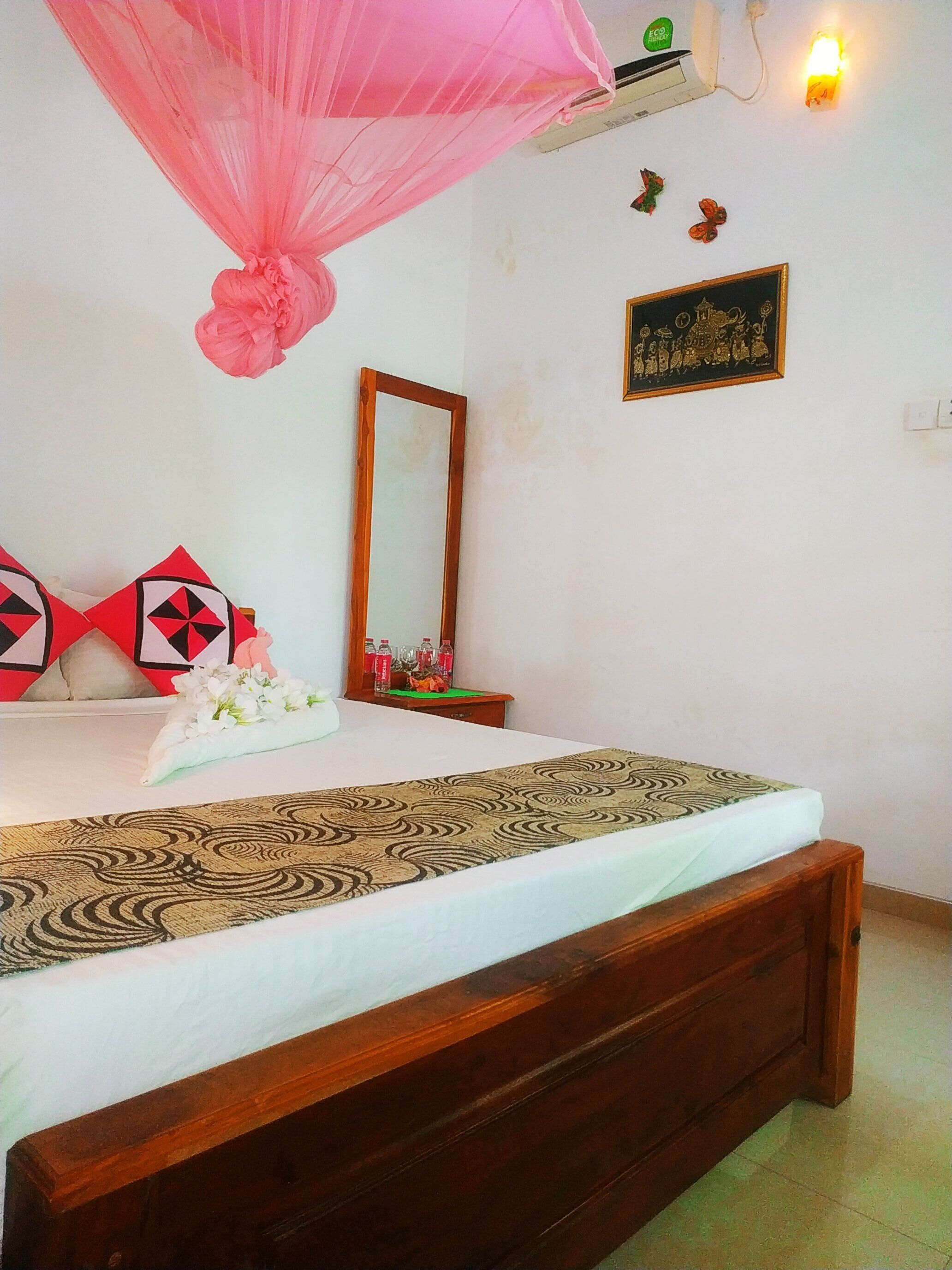 A neatly made bed with a patterned bedspread, a wooden headboard, and a bedside table with a mirror and decorative items.