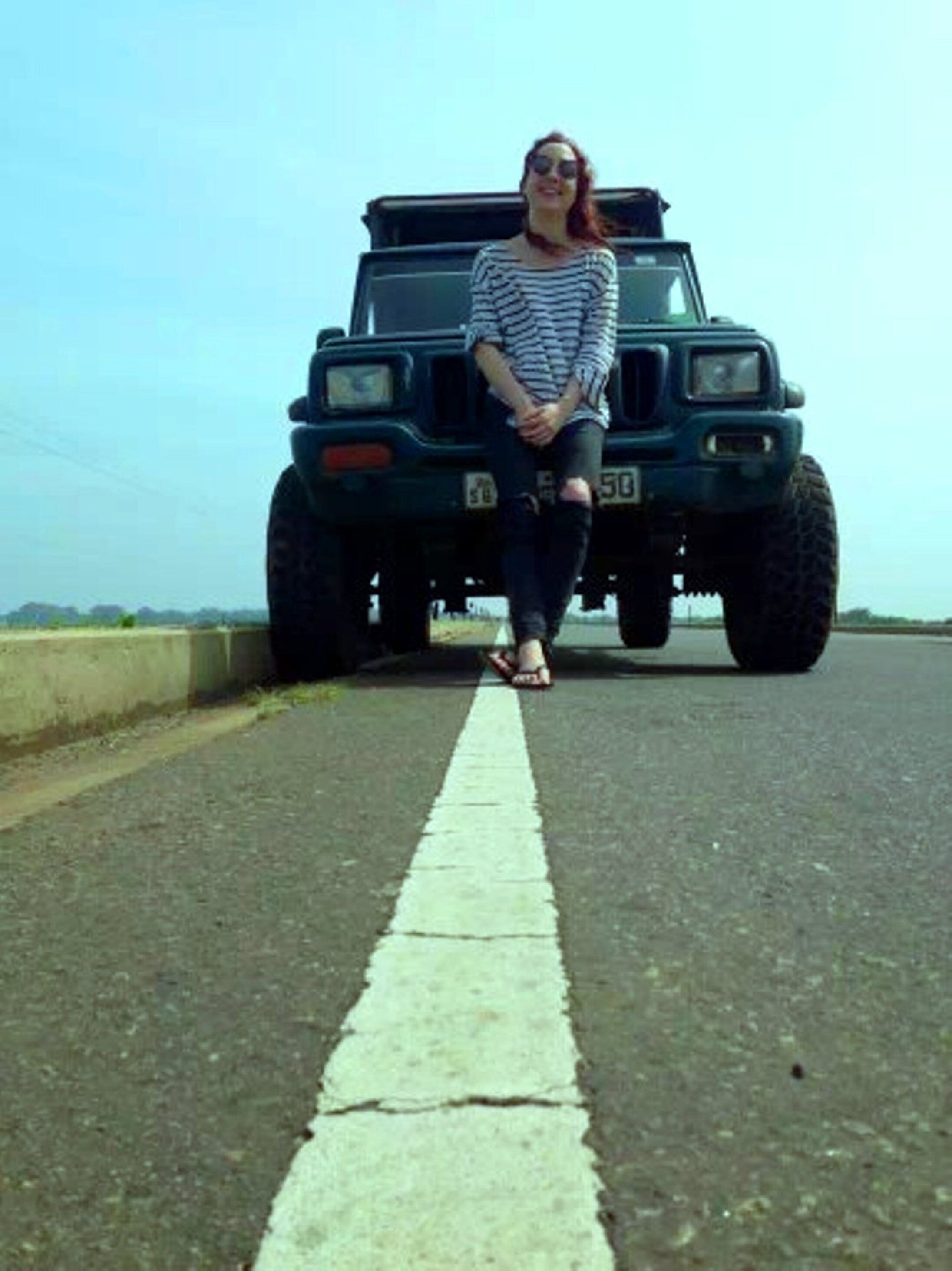 A person sitting on a road with a large vehicle in the background.