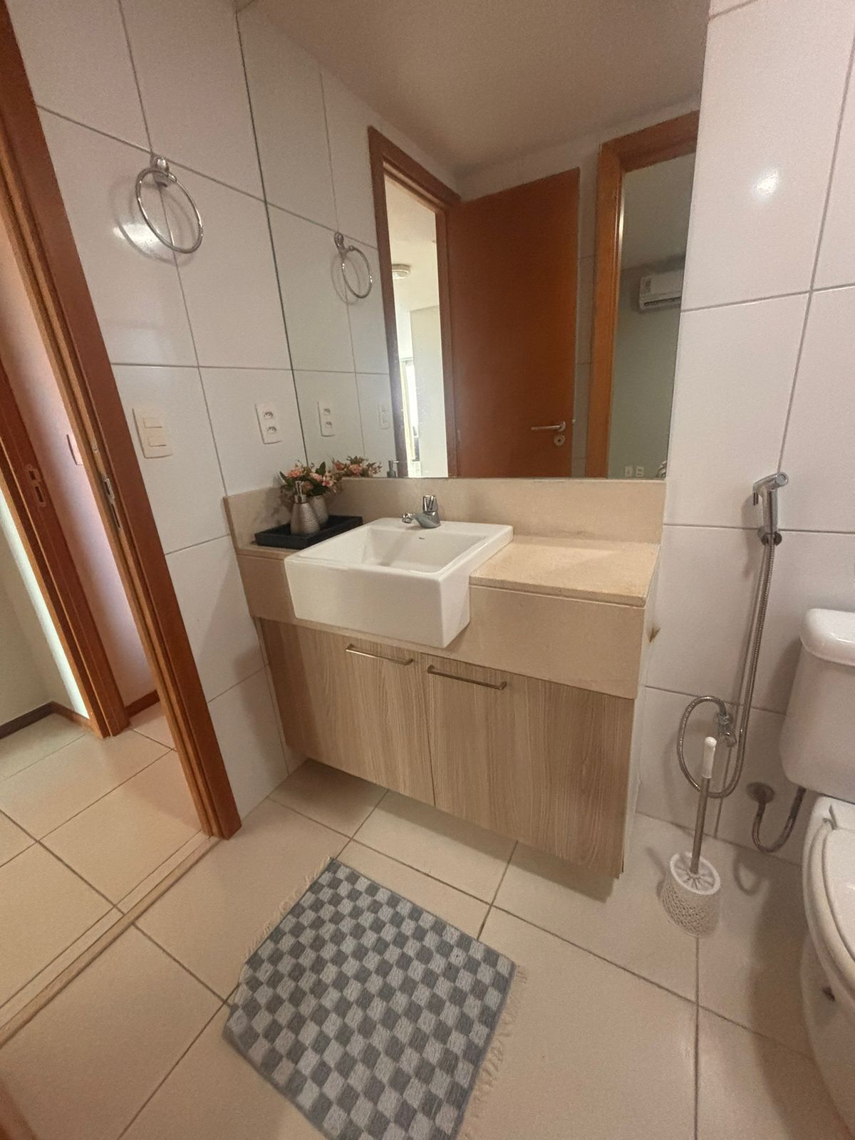 Un baño con lavamanos blanco, armarios de madera, un espejo y una ducha.