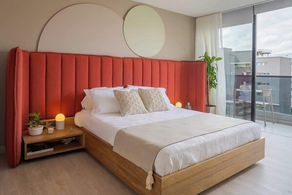Une chambre moderne avec un lit en bois, une tête de lit rembourrée rouge, des tables de chevet ornées de plantes et une grande fenêtre donnant sur la ville.