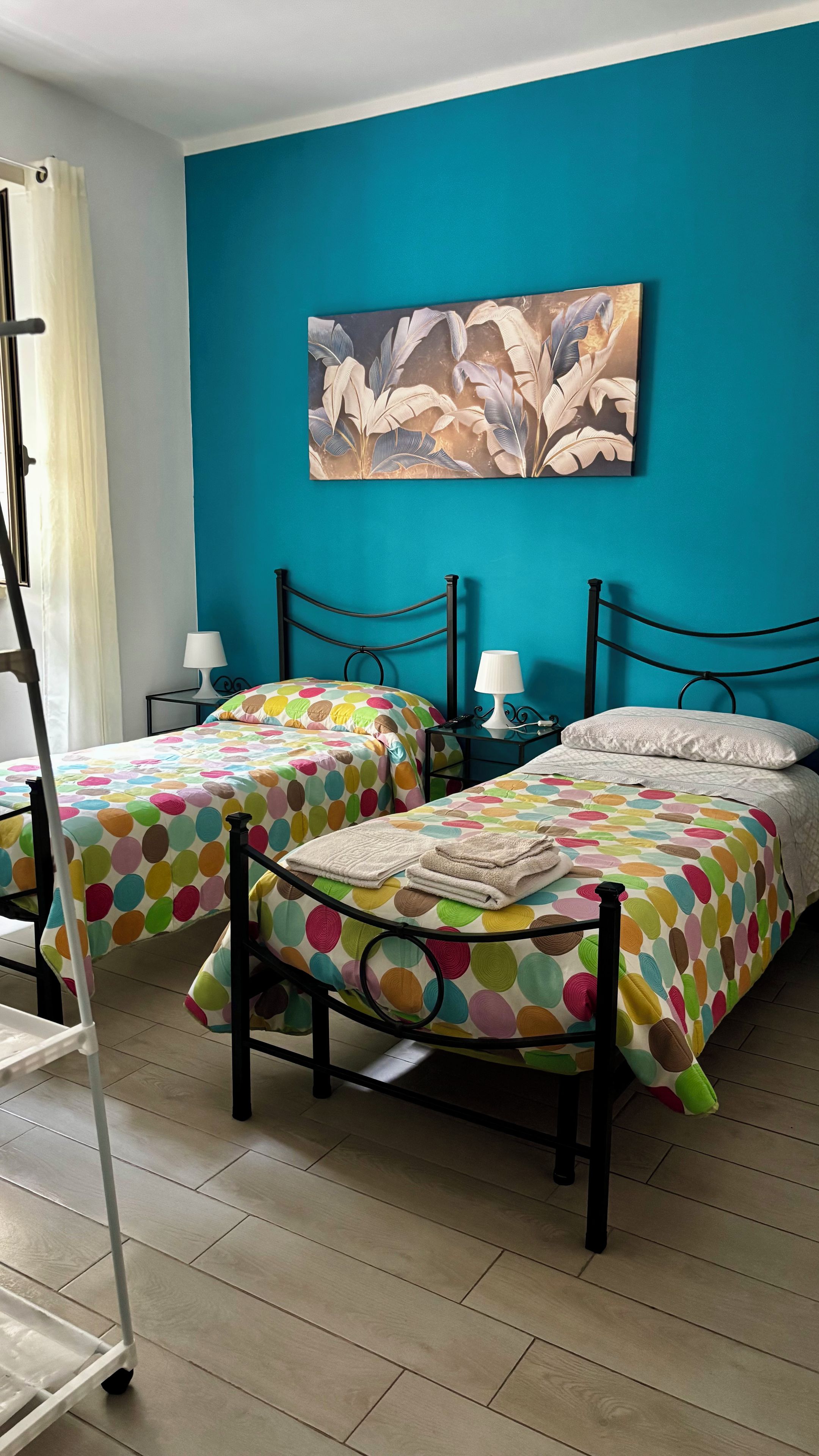 A room with two beds, each with a polka dot bedspread, a nightstand with a lamp, and a wall with a large abstract painting.