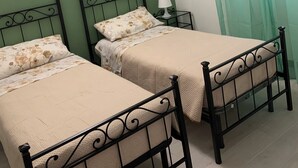 Een kamer met twee eenpersoonsbedden, een nachtkastje met een lamp en een raam met groene gordijnen.