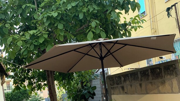 Een terras buiten met een houten tafel, twee krukken en een grote parasol.