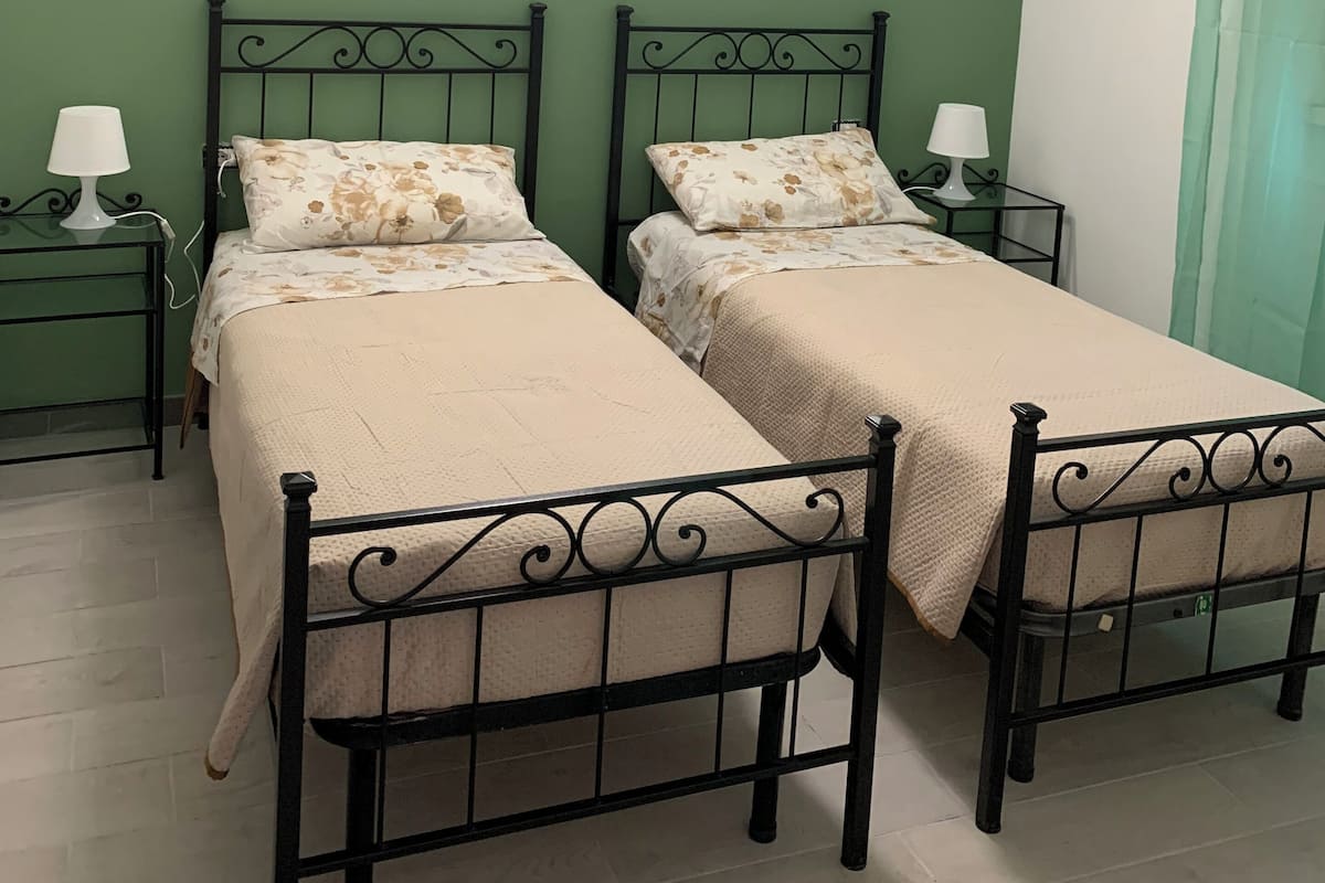 A room with two beds, green walls, and a single light fixture.