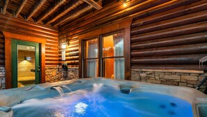 A log cabin with a hot tub, stone walls, and a wooden ceiling.
