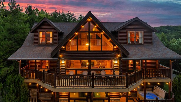 A log cabin with multiple levels, a balcony, and a hot tub.
