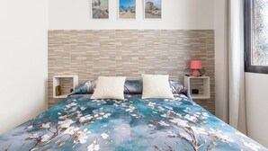 Un dormitorio con cama, dos mesitas de noche, una lámpara de noche, una ventana y tres cuadros en la pared.