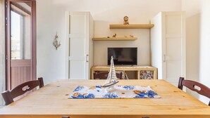 Un comedor con una mesa de madera, sillas, un modelo de velero, un televisor y una repisa decorativa con figuritas.