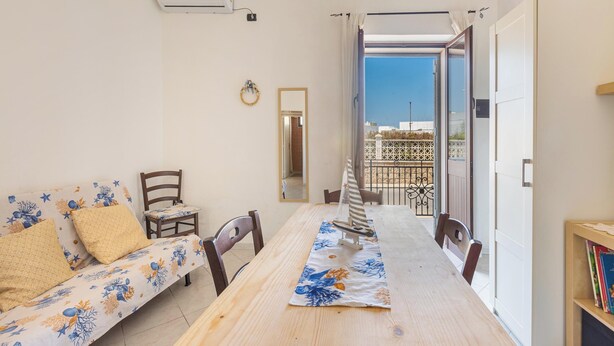 Una habitación con una mesa de comedor de madera, un sofá estampado con motivos florales, una pequeña silla de madera y una estantería.