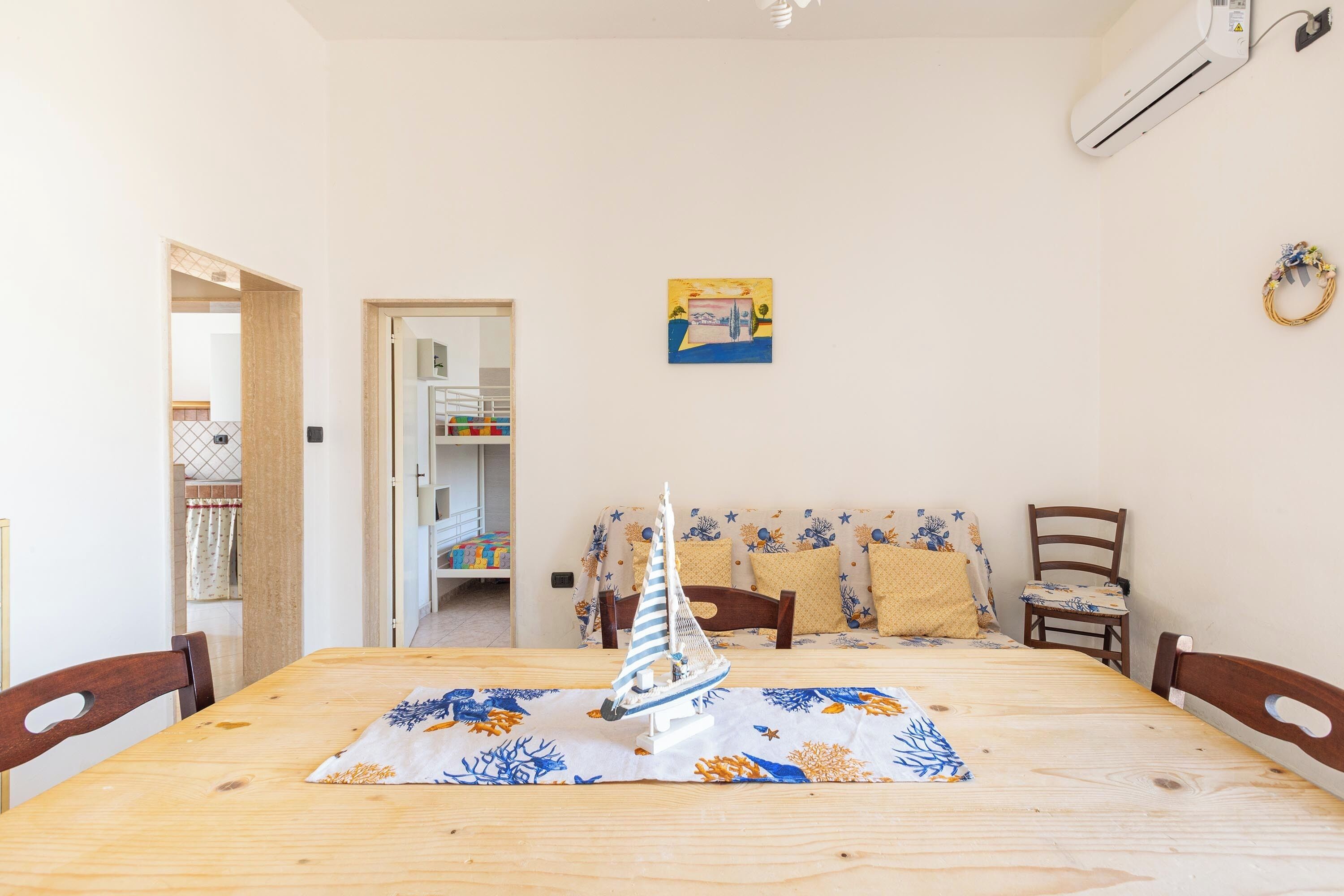Un comedor con una mesa de madera, sillas, un modelo de velero y un sofá con cojines.