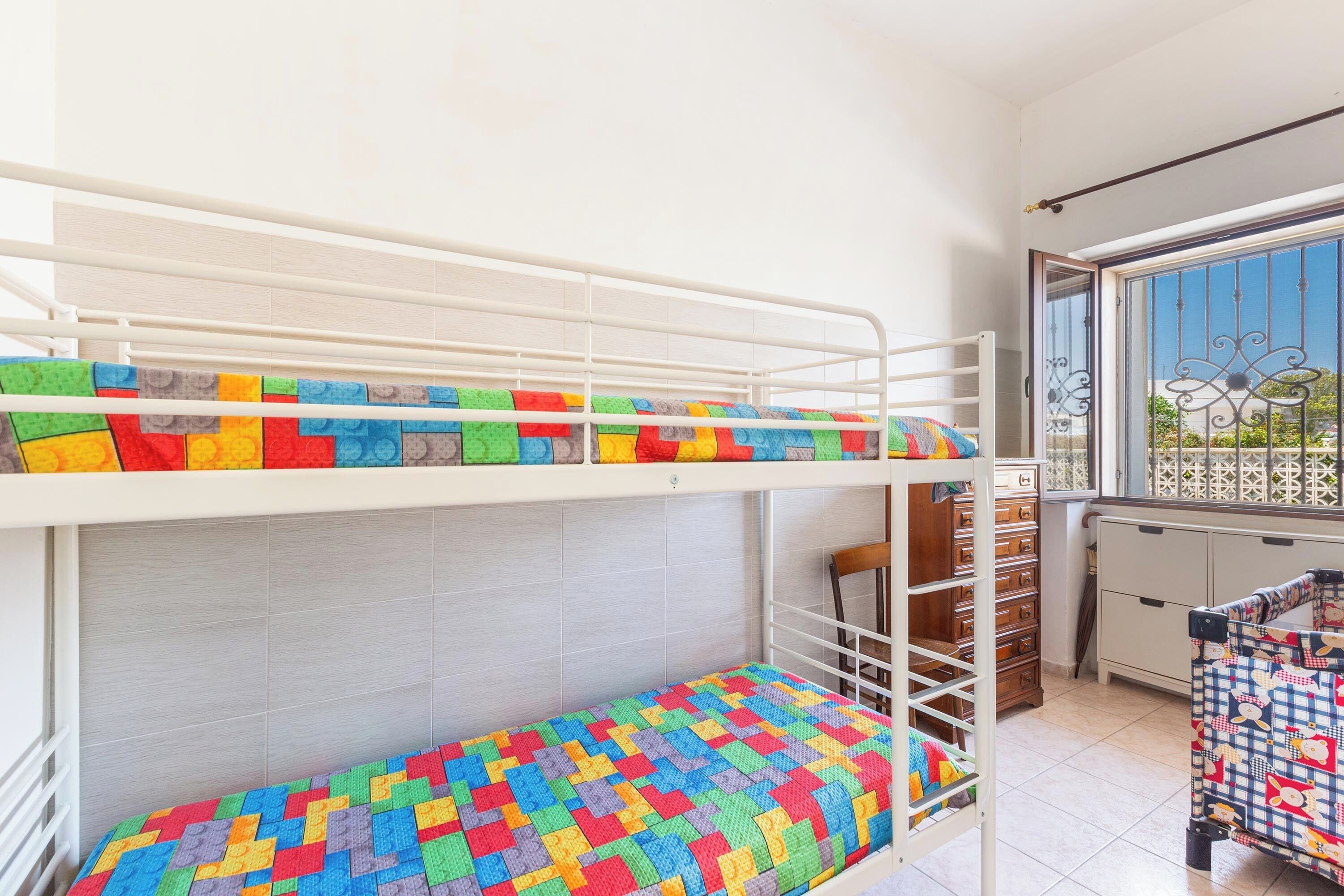 A bunk bed with colorful bedding, a window with a view, and a small kitchenette area.