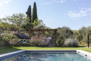 Relax by the serene pool surrounded by a lush garden and shaded pergola.