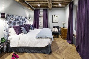 Relax in this serene bedroom with a large bed, wooden floor, and rustic ceiling, featuring a dresser and a small table with a vase of flowers.