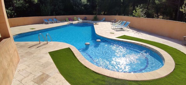 Una piscina con un pequeño jacuzzi, rodeada por una terraza con sillas de descanso.
