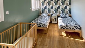 A room with two single beds, a wooden crib, and a patterned wall.