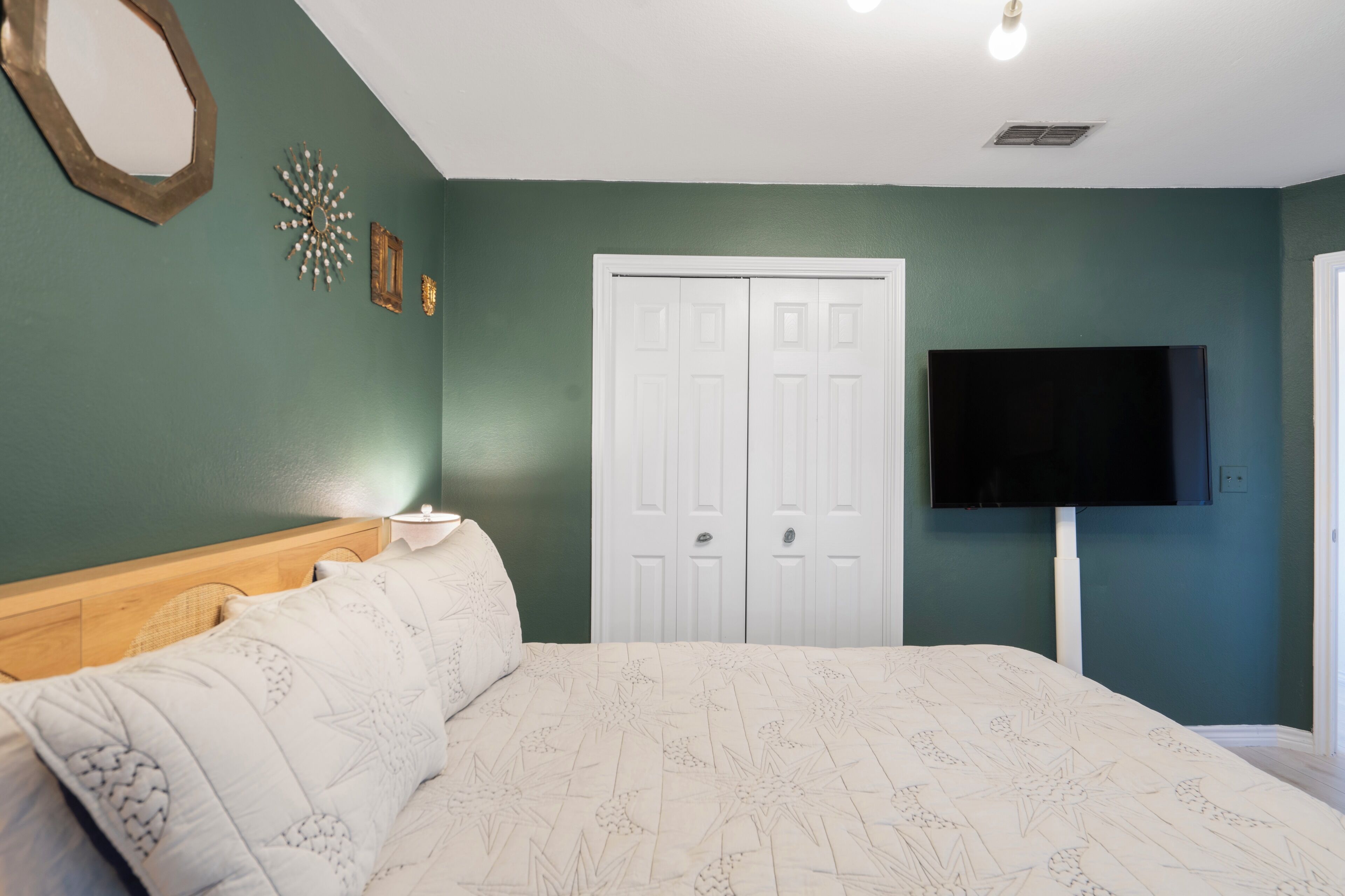 Une chambre avec un lit, une armoire blanche et un téléviseur fixé au mur.