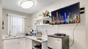 Una cucina compatta con forno a microonde, tostapane e frigorifero. Una TV a schermo piatto montata a parete mostra una vista sulla città.