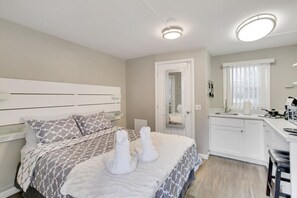 Une chambre comprenant un lit, une table de chevet et une petite kitchenette équipée d’un évier et d’un plan de travail.