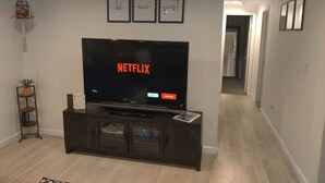 Uma sala de estar com televisão de tela plana em um suporte de madeira escura, uma pequena planta em uma prateleira e três quadros na parede.