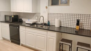 Cozinha com armários brancos, bancada preta, pia, micro-ondas e lava-louças.
