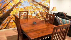 Uma área de refeições com mesa e cadeiras de madeira, uma luminária e um sofá com almofada estampada.
