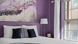 Une chambre à coucher avec un lit, des oreillers, une table de chevet, une lampe et une fenêtre.