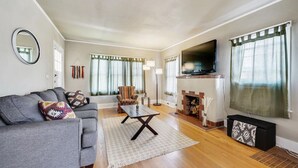 A living room with a grey sofa, patterned cushions, a coffee table, a fireplace, and a TV mounted on the wall. - Golden Luxe Bungalow | Walk to Downtown & Parks (Golden)