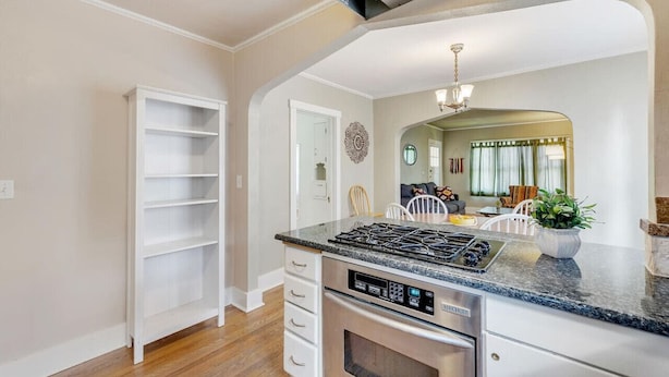 A kitchen with a built-in stove, white cabinetry, and a dining area visible through an archway. - Golden Luxe Bungalow | Walk to Downtown & Parks (Golden)