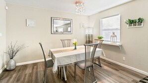 Un coin repas comprenant une table, des chaises, un vase de fleurs, un miroir et une fenêtre avec des stores.