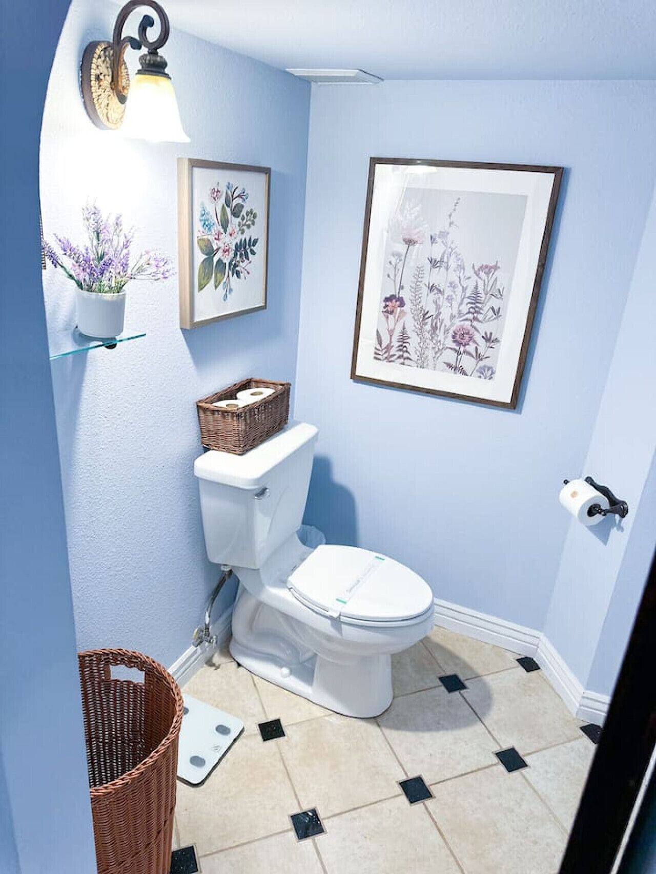 Ein Badezimmer mit Toilette, Waschbecken, einem Korb und gerahmten Blumenbildern an den Wänden.