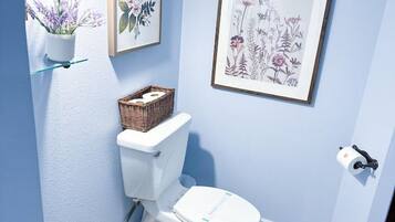 Ein Badezimmer mit Toilette, Waschbecken, einem Korb und gerahmten Blumenbildern an den Wänden.