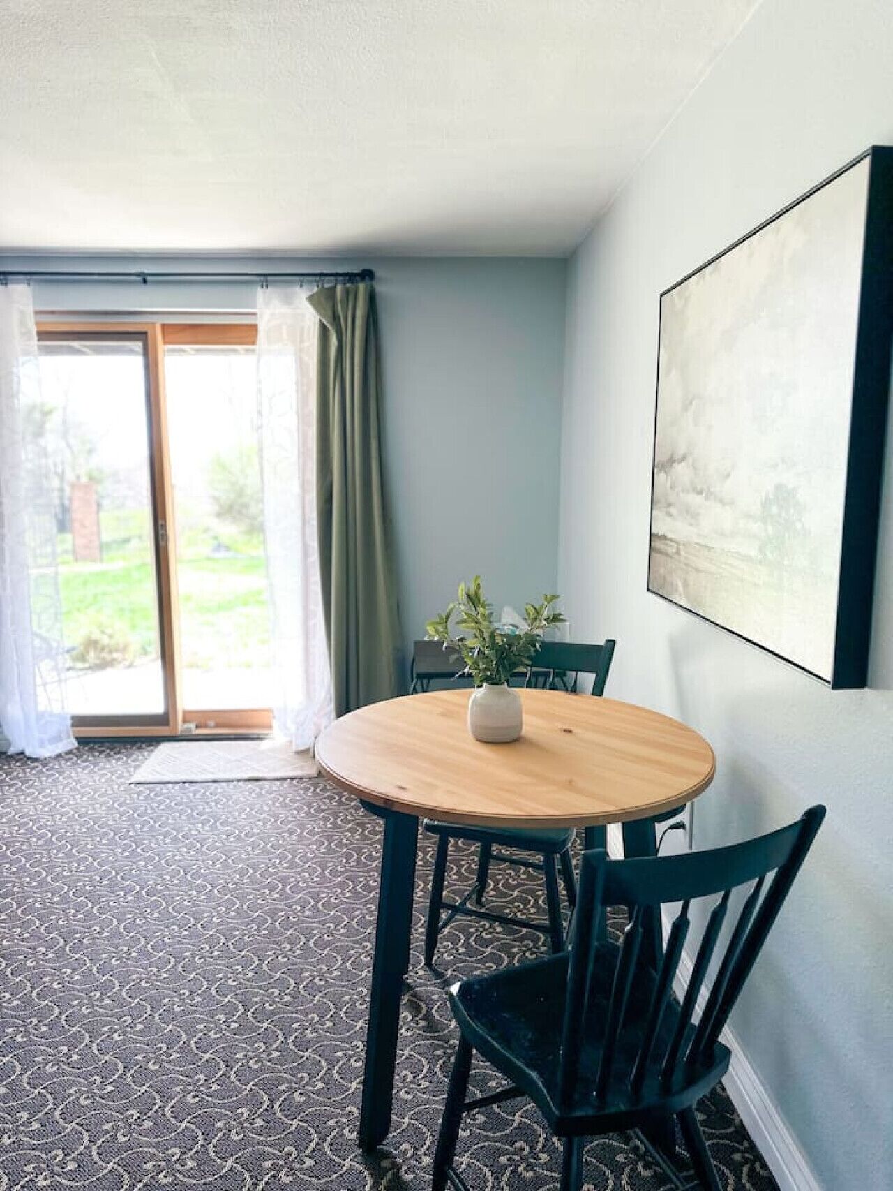 Ein Zimmer mit einem runden Holztisch, zwei Stühlen, einem Blumentopf und einem großen gerahmten Bild an der Wand.