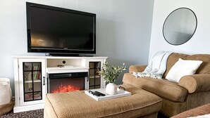 Hotellihuoneessa on seinälle asennettu litteänäyttöinen televisio takan yläpuolella, sohva ja pyöreä peili seinässä.