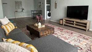 A living room with a gray sofa, a wooden coffee table, a TV stand, and a patterned rug. - Lakewood Gem: Furnished Haven! Perfect for Month Long Stays! (Lakewood)
