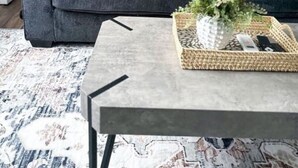 Una sala de estar moderna con un sofá gris, una mesita de centro con una bandeja tejida y una lámpara de pie.