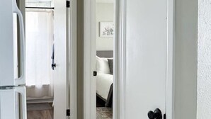 Un estrecho pasillo con suelo de madera que conduce a un dormitorio con cama y mesita de noche.