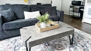 Una sala de estar con un sofá gris, una mesa de centro con una bandeja tejida y una alfombra estampada.