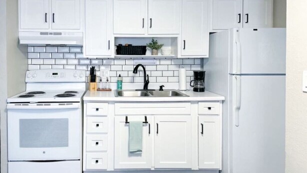 Una cocina con armarios blancos, estufa blanca, un lavaplatos y un refrigerador.