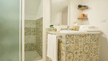 A bathroom with a tiled wall, a sink, a mirror, and a shower area.