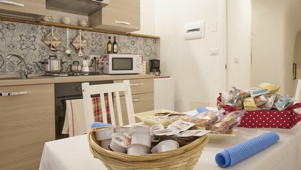Une cuisine équipée d’un four à micro-ondes, d’une cuisinière et de divers ustensiles. On y trouve un panier en osier rempli de vaisselle et une serviette bleue posée sur la table.