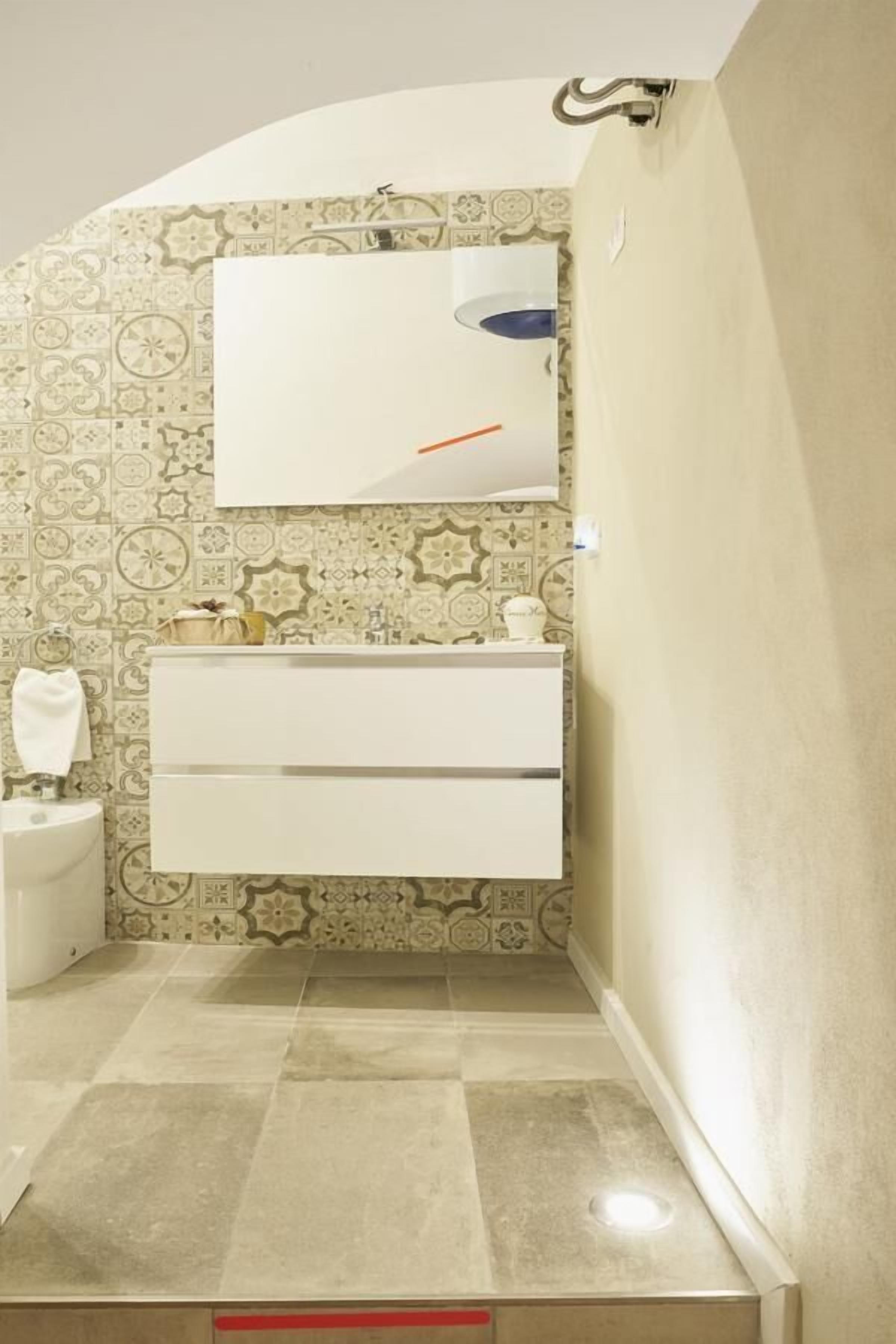 A bathroom with a white vanity, a mirror, and patterned tile walls.