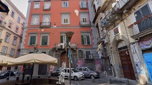 Une rue étroite bordée d’un immeuble à la façade rouge et doté de nombreuses fenêtres.