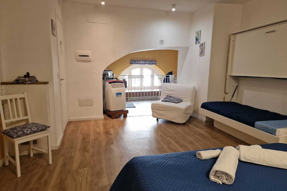 A bedroom with two beds, a white chair, a heater, and a view of a balcony.